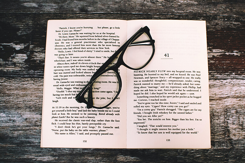 A set of eyeglasses placed on top of an open book of essays